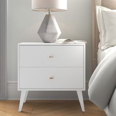 a nightstand with a lamp on top of it next to a white bed in a bedroom