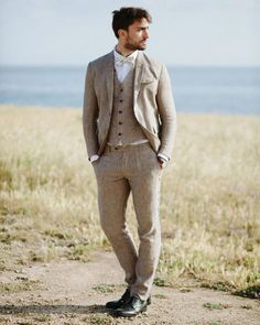 a man in a suit and tie standing on a dirt road near the ocean with his hands in his pockets