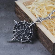 a silver compass necklace sitting on top of a wooden box