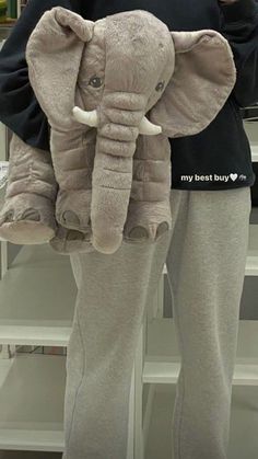 an elephant stuffed animal sitting on top of a person's leg wearing sweatpants