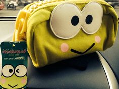 a green bag with eyes and nose on top of a car dashboard next to a sticker