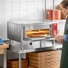 a man standing in front of an oven with a pizza on the counter and some boxes under it