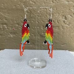 a pair of colorful parrot shaped beaded earrings sitting on top of a glass stand