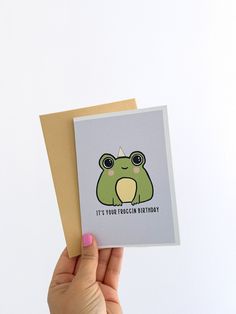 a hand holding up a card with a frog on it's face and the words, it's your trachen birthday