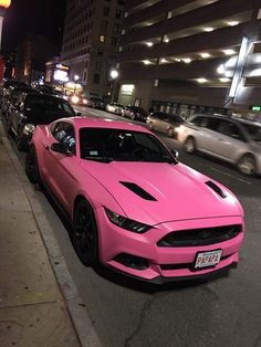 a pink car is parked on the side of the road in front of some cars