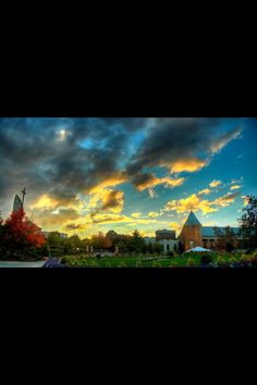 the sun is setting over a church and trees in front of it, with colorful clouds