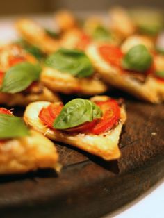 small appetizers are arranged on a wooden platter with green and red toppings