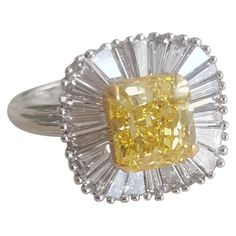 This understated, elegant and enticing ring created by Moguldiam Inc in 18 k white gold features a GIA certified natural fancy vivid yellow Radiant weighing 2.02 carat with VS2 clarity with a halo of tapered baguette accent diamonds weighing 1.10 carat with GH color and VS clarity. The ring size is 7 and is sizable as per requirement. The gold weight is 4.42 grams.