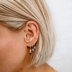 a woman with blonde hair wearing two gold ear cuffs and an earring that has three small bars attached to it