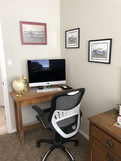 a desk with a computer on top of it next to a wooden dresser and framed pictures