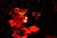 several different types of cocktails on a table in a dimly lit room with menus and wine glasses