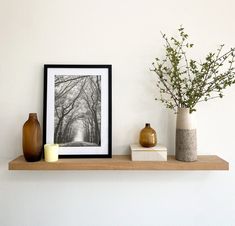 two vases with flowers are sitting on a shelf in front of a framed photograph