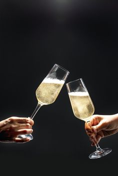 two people toasting with champagne glasses in front of a black background and one person holding out their hand