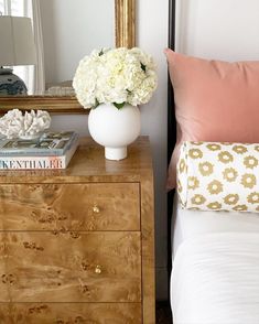 a white vase filled with flowers sitting on top of a wooden dresser next to a mirror