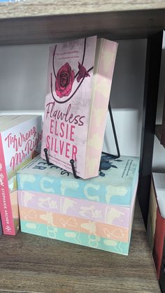 a stack of books sitting on top of each other next to a book case with a pink rose