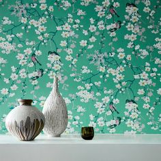 two vases sitting on a shelf in front of a wallpapered with flowers