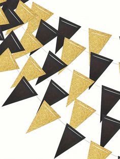 black and gold party flags with glitter triangles hanging from the ceiling in front of a white wall