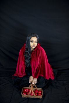 a woman sitting on the ground with apples in her hand and wearing a red cloak