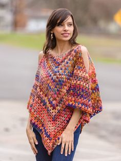 a woman wearing a multicolored crocheted ponchy with her hands on her hips