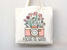 a tote bag with flowers and a camera printed on the front that says focus on the good