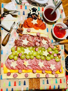 a platter filled with meat and cheeses next to crackers, olives, grapes, bread