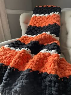 an orange and black crocheted blanket sitting on top of a white chair