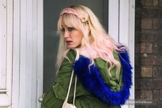 a woman with blonde hair and blue fur vest carrying a white bag in front of a door