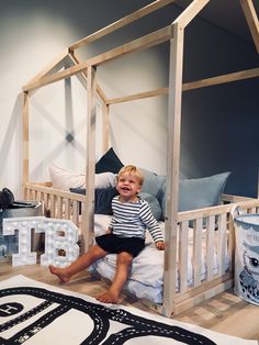 a young boy sitting on top of a bed next to a wooden canopy over it