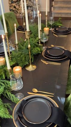 the table is set with black plates and gold trimmings, greenery and candles