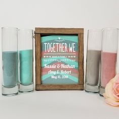 three shot glasses with sand in them next to a framed sign that says together we make family