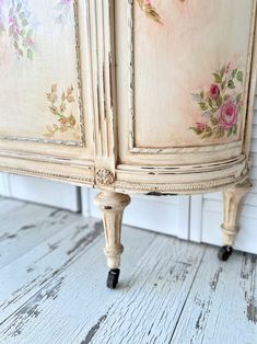 an old dresser painted with floral designs on the doors and drawer pulls, sitting on a white wooden floor