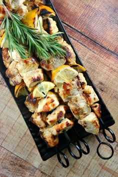 chicken kabobs with lemons and rosemary garnish on a black tray