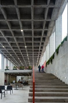 two people are walking up some stairs in an open area with concrete walls and flooring