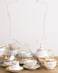 an assortment of tea cups and saucers on a table with a white wall in the background