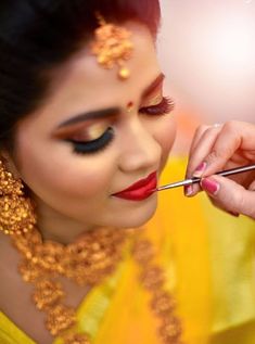 a woman is getting her make up done with gold and red makeup, while holding a pair of scissors