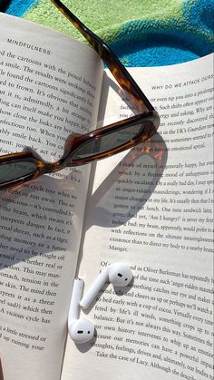 an open book with glasses and earbuds laying on it next to a pair of reading glasses