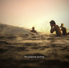 three people in the ocean with surfboards under their arms, one on his knees