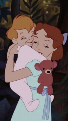 two children hugging each other in front of trees and bushes, one holding a teddy bear