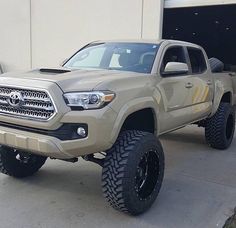 a tan toyota truck parked in front of a building with two large tires on it