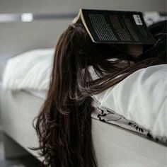 a woman laying on top of a bed with a book on it's head