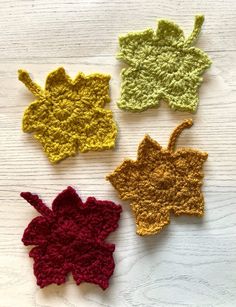 four crocheted leaves on a white wooden surface, one is yellow, the other is red