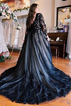 a woman in a black dress standing on a wooden floor next to some wedding gowns