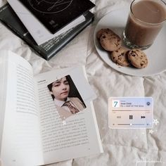 an open book next to some cookies and a glass of coffee on a bed with white sheets