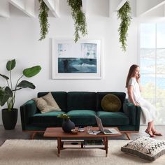 a woman standing next to a green couch in a living room with potted plants