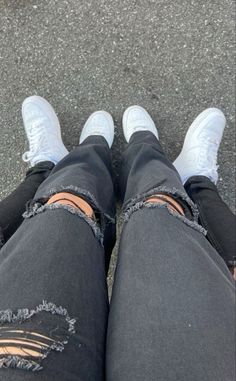 the bottom view of someone's legs with ripped jeans and white shoes, looking down at their feet