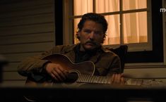 a man sitting in front of a window holding a guitar