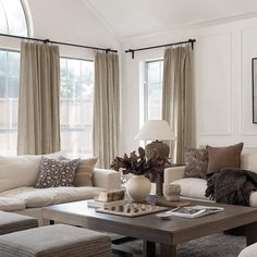 a living room filled with lots of furniture next to two large windows covered in curtains