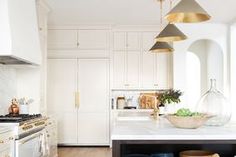 a kitchen with white cabinets and marble counter tops, gold pendant lights over the island