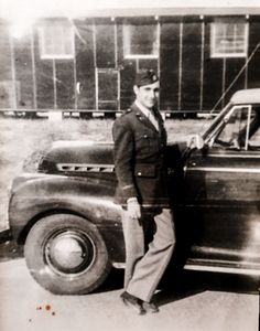 an old black and white photo of a man in uniform standing next to a car