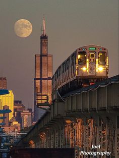 a train traveling over a bridge with the moon in the sky and buildings behind it